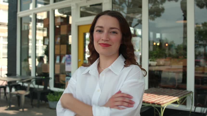 Woman smiles while posing in front of a cafe with reflective windows