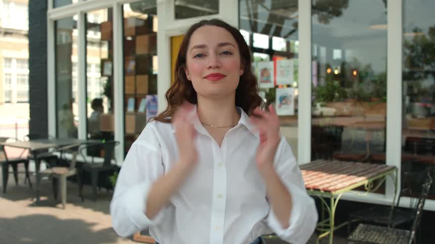 Woman crosses her arms and smiles in front of an outdoor cafe