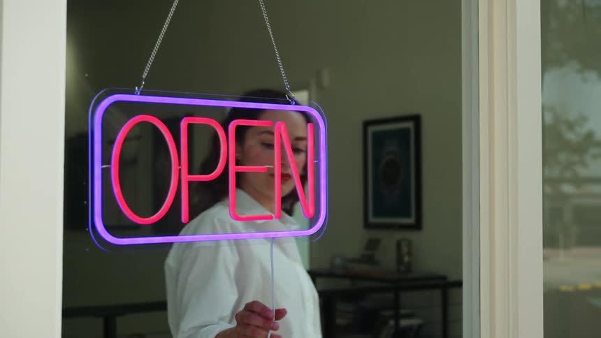 Woman turning off the neon open sign in a store window