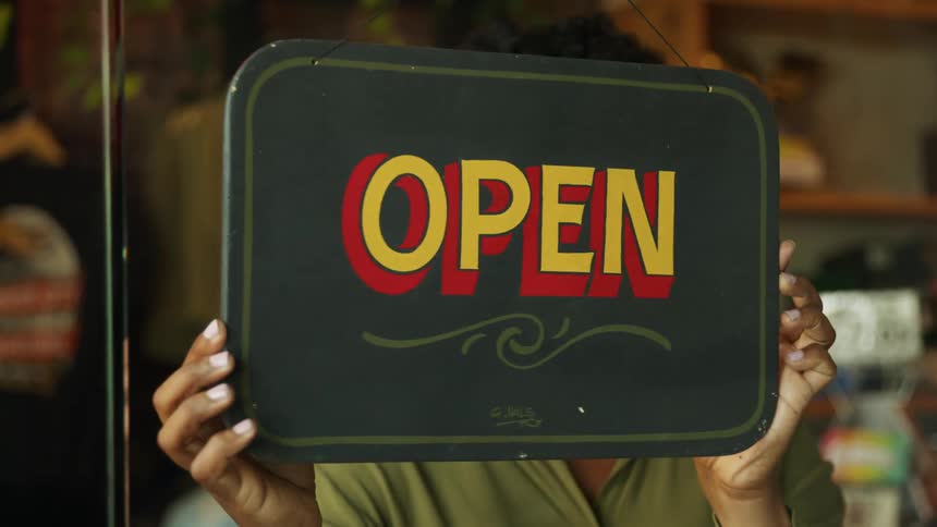 Woman turning the sign to open on the window of a commercial establishment