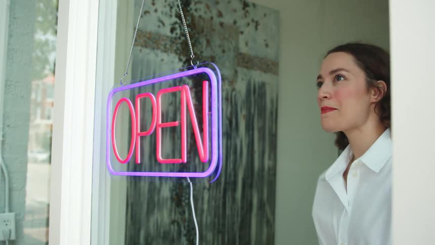 A woman turns on an open sign in a shop window