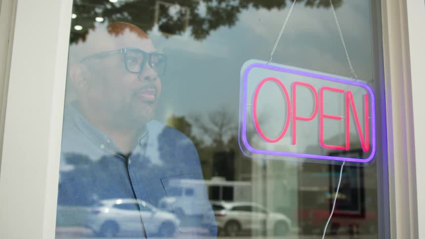 Man turning on the open sign in the window of a store in a commercial establishment