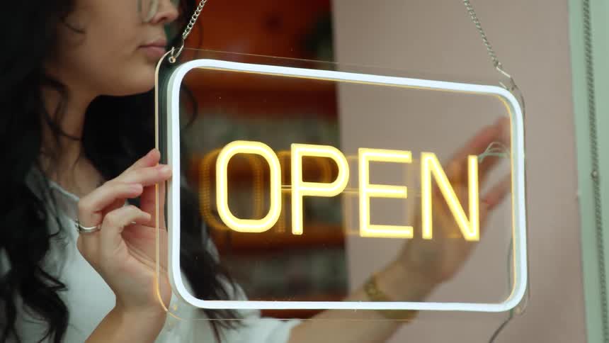 A woman turns on the neon open sign hanging in the window