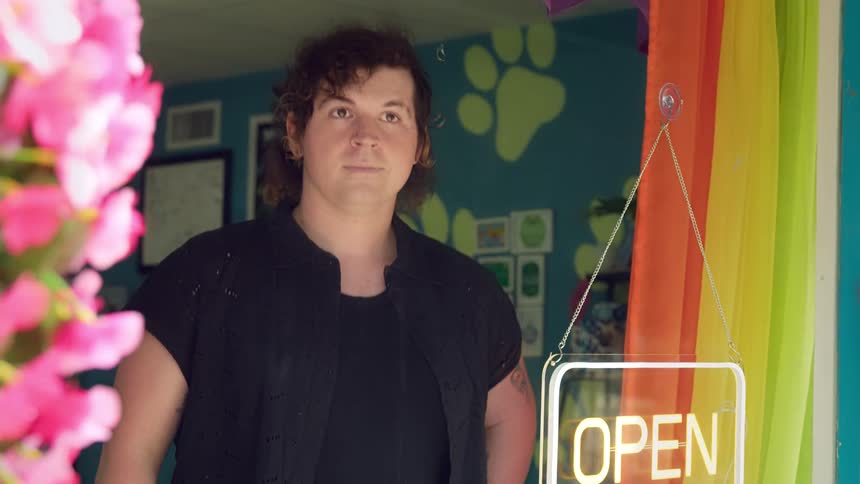 A man in a pet shop turns on the open sign and gazes out the window