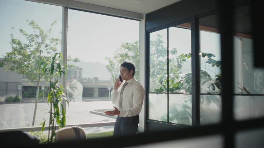 A man dressed formally talks on the phone and walks around his office