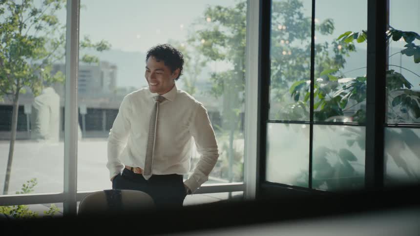 Happy businessman quietly celebrates at the office in a room with windows looking out at a busy highway