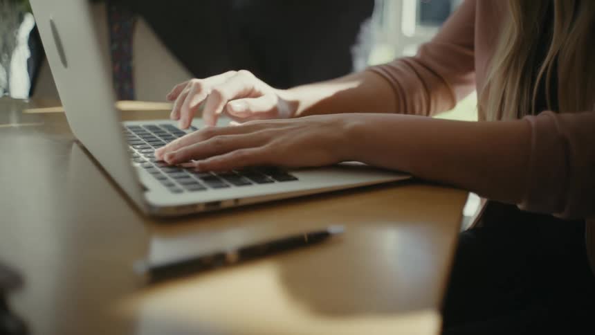 Hands of a woman typing on a laptop on top of an office desk