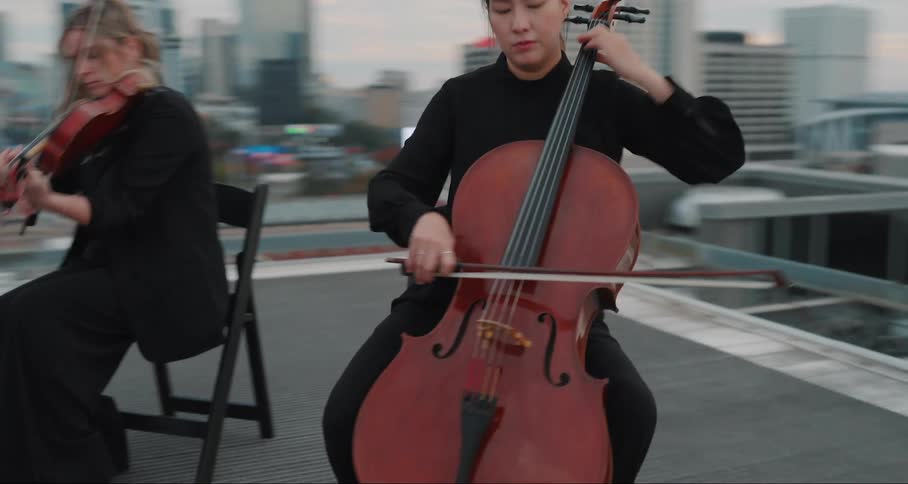 Musicians play string instruments while sitting on a rooftop in the city after dusk