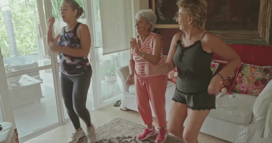 Three women in workout attire dancing in a welllit living room
