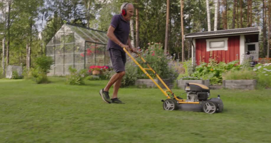 An elderly man mowing the lawn with a yellow and black lawnmower in front of a red house