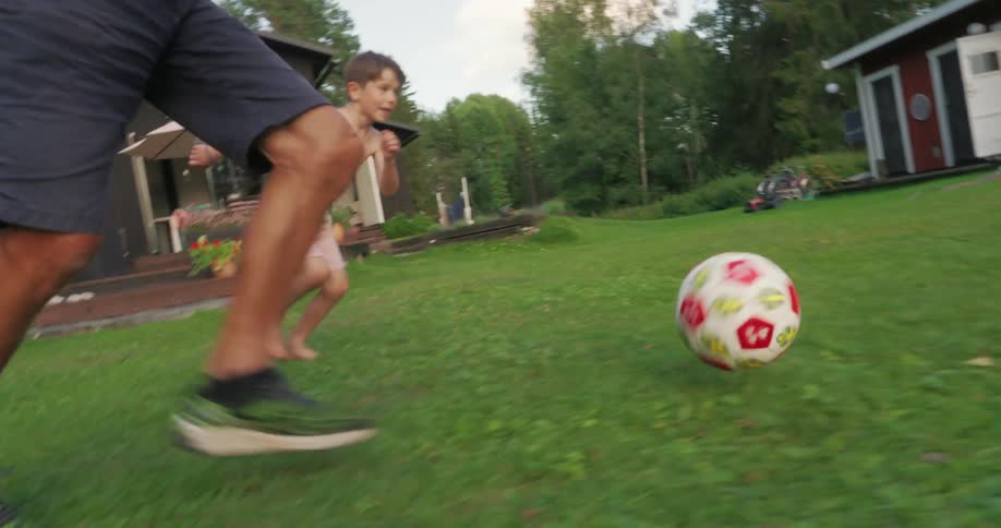 Grandad playing ball with his grandson in the backyard with grass and trees in the background