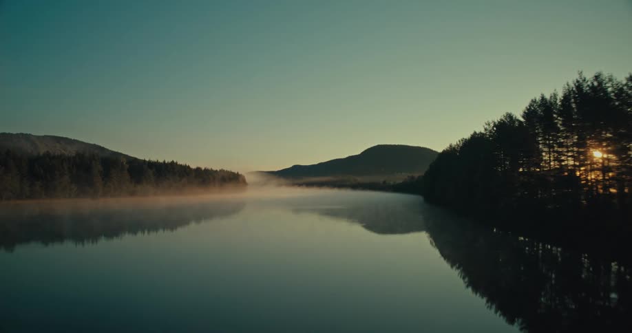 A serene lake reflecting the surrounding mountains and trees at dawn