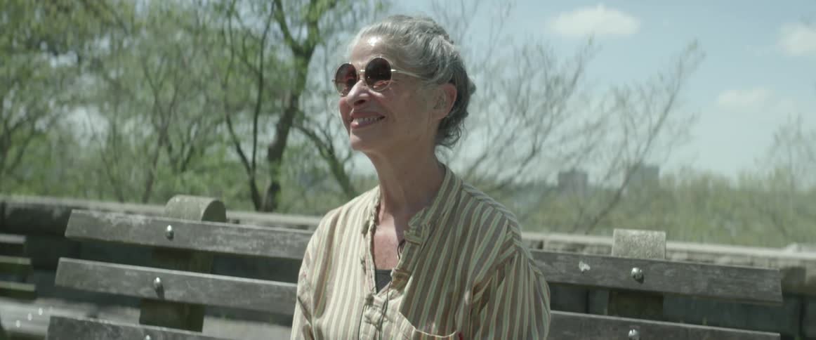Older woman in sunglasses sitting outside on bench and smiling