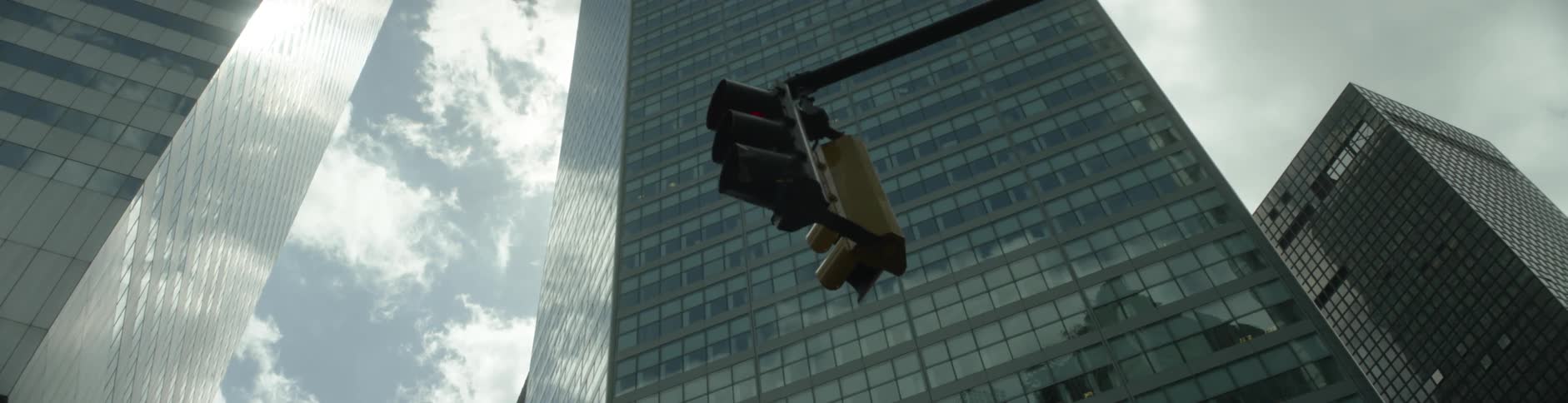 A street light shining red hangs in front of a skyscraper