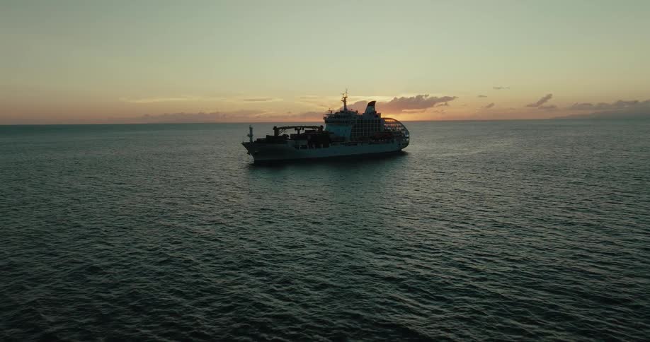 Large ship sailing across the sea with the sun on the horizon