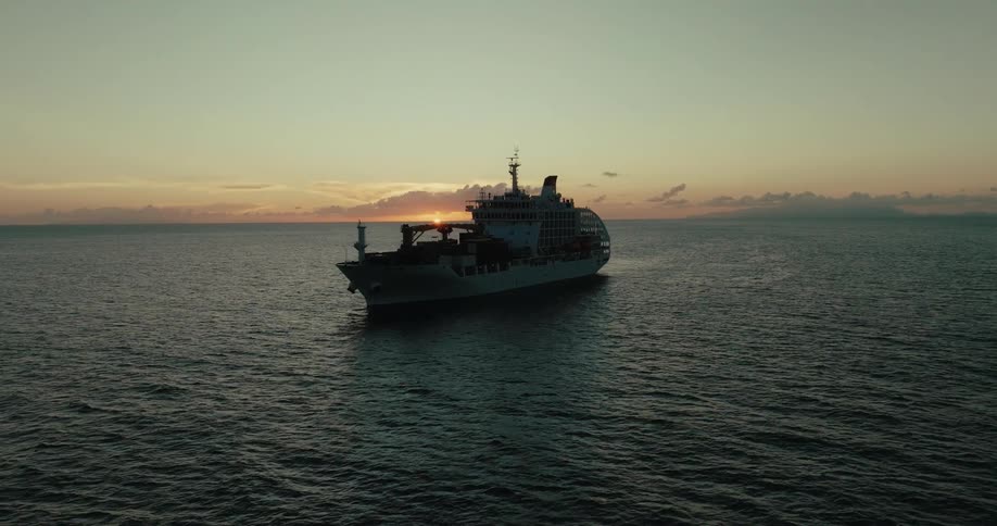 Cargo ship traveling at sea with the sun setting on the horizon
