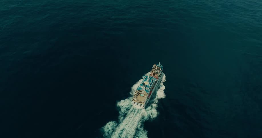 A large cruise ship sails through deep blue ocean waters creating white waves as it moves