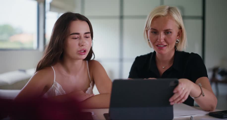 Two women sitting at a table refer to a computer during a discussion