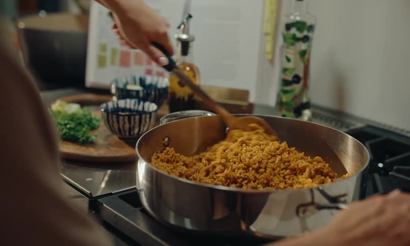 Person is stirring a large pot full of yellow rice on the stove