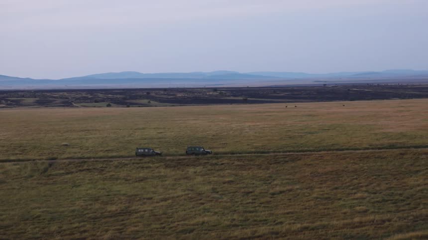 Two vehicles traverse a vast flat grassland on a road that cuts through the terrain