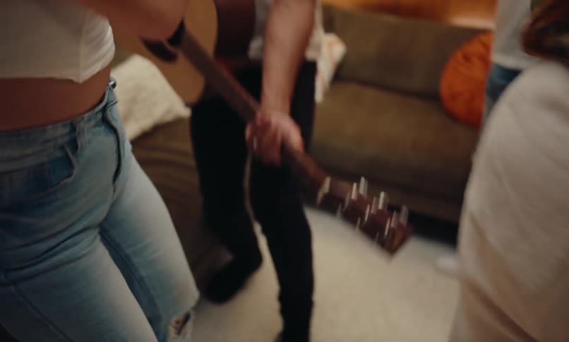 A group of friends dancing at an indoor party in an apartment with warm lighting and wooden furniture