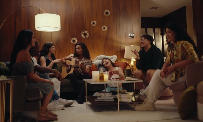 A group of friends gathered and sitting on a sofa talking and one of them is holding a guitar in his hand