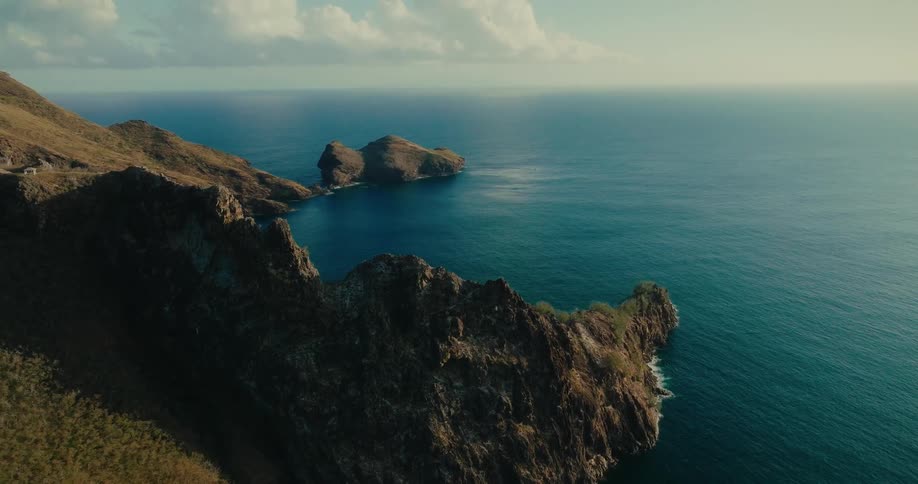 A rugged cliff overlooking a calm blue ocean with rocky promontories near the shore