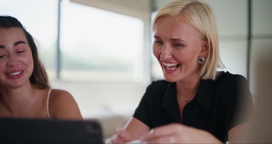 Coworkers sitting in a meeting room laugh while working with a computer