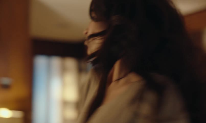 A woman dancing alone in an apartment with warm lighting and wooden furniture
