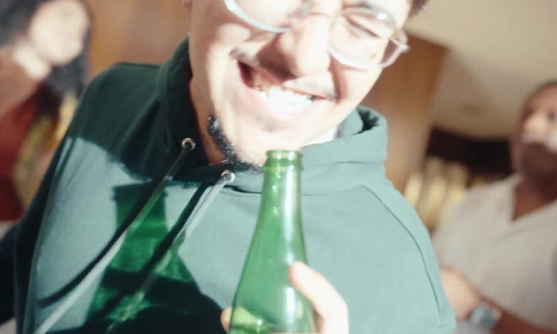 A man with closed eyes is happy and singing using a green glass bottle as a microphone and a strong light hits his face