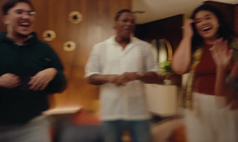 A group of friends dancing at an indoor party in an apartment with warm lighting and wooden furniture