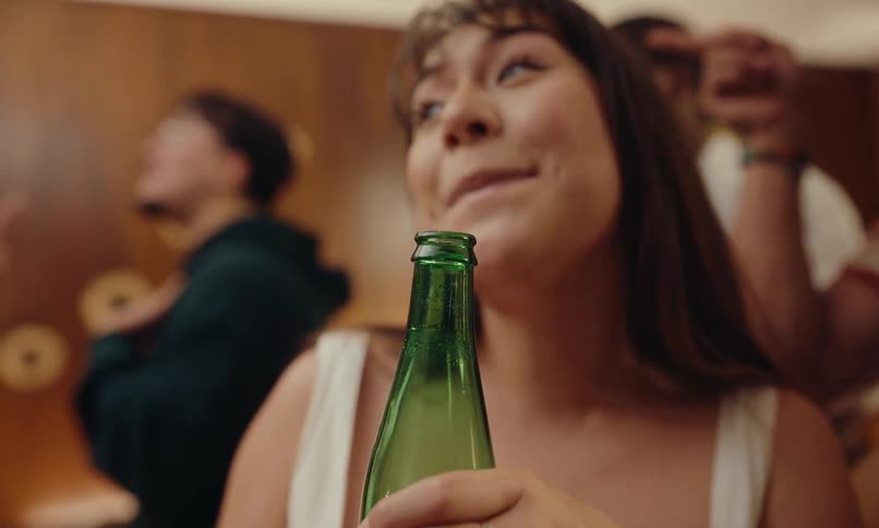 A woman holding a green beer bottle and she is singing happily