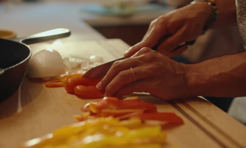 A persons hands slice bell peppers on a wooden cutting board with a knife