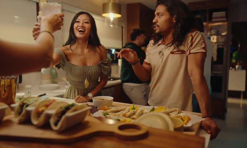 Group of friends talking in the kitchen of a house and toasting with glasses and tortillas on the table