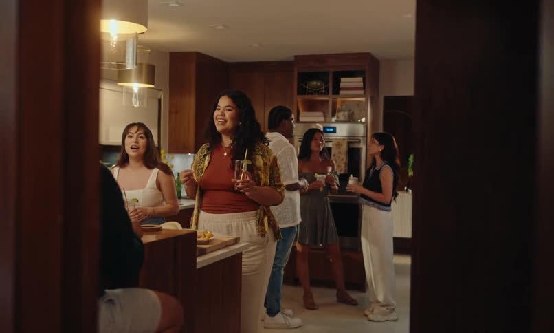 Group of people talking and holding drinks at a celebration in the kitchen part of a house at night