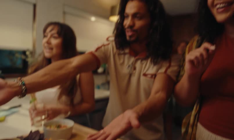 A group of friends talking in front of a table full of food and two people clink their glasses