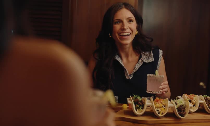 Woman sitting at table smiling holding a drink and food on the table