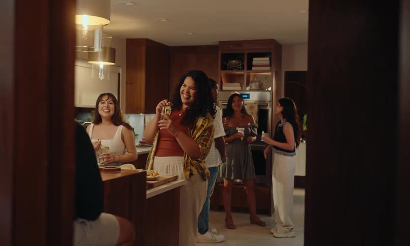 Group of friends in a house kitchen talking and holding drinks at a party