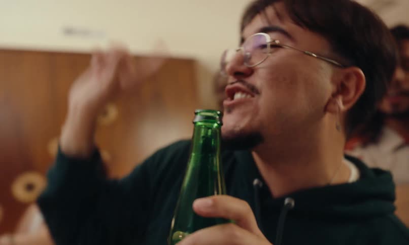 A man with glasses holding a green glass bottle and singing to it and he is happy