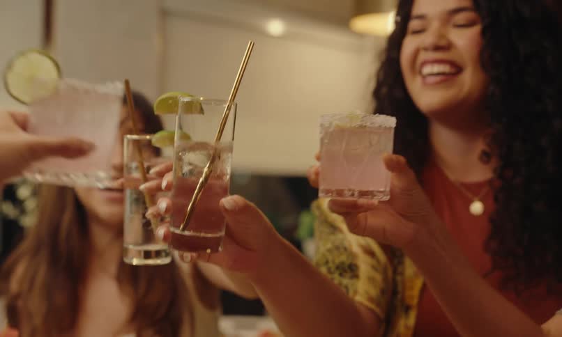 Friends in the kitchen with food on the table and holding drinks toasting