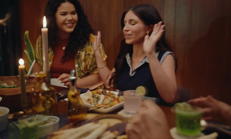 Some people gathered around a table with food and a woman is talking and smiling