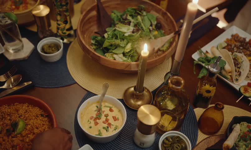 A dinner table with various dishes including a large wooden salad bowl small bowls of sauces and lit candles