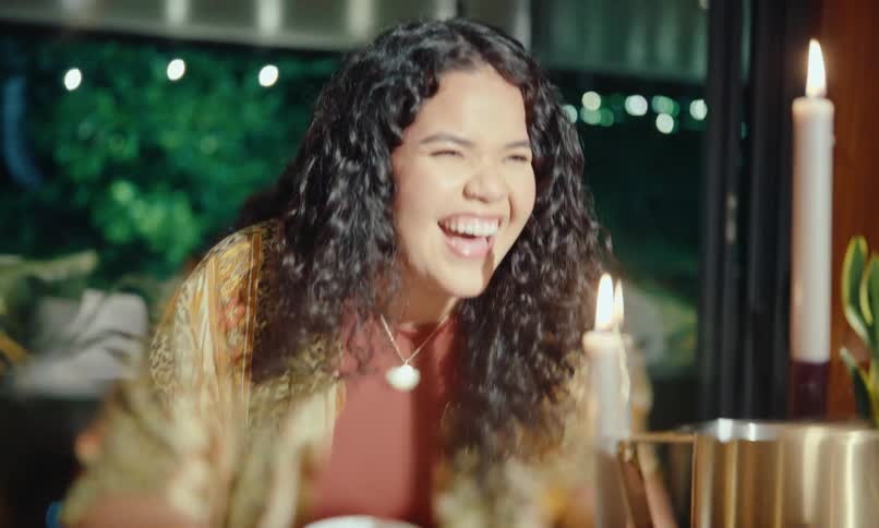 A young woman smiles and laughs happily at a dinner party while a camera flash goes off
