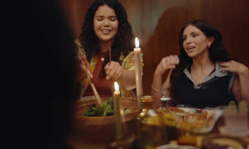 Group of friends sitting at a dinner table with candles serving themselves while chatting happily