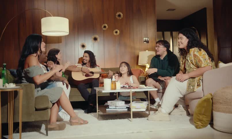 Friends sitting in the living room chatting at a celebration with one of them holding a guitar