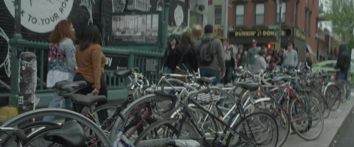 People walk past a bunch of parked bikes in the city