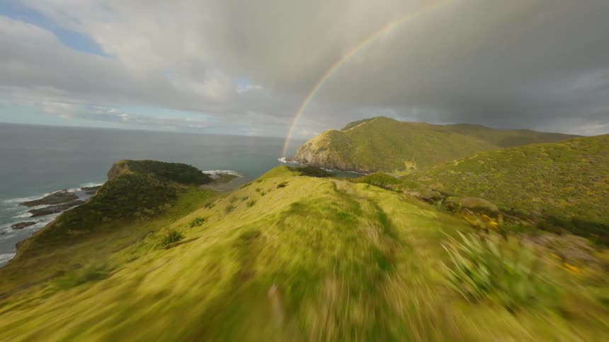 Aerial view of a mountainous valley by the sea with a cloudy sky and a rainbow in the background