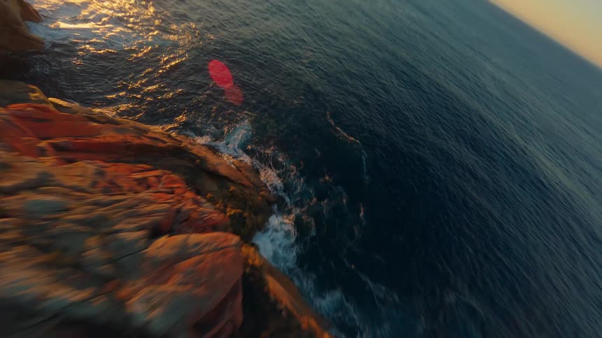 An aerial view of a rugged coastline with cliffs and promontories stretching alongside the ocean as the sun sets
