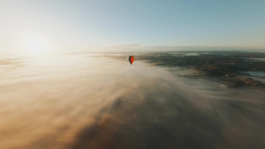 Aerial view of a colorful balloon on the horizon above a sea of clouds against a blue sky