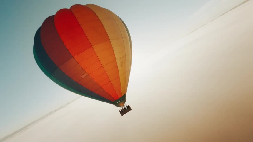An orbiting aerial view of a colorful hot air balloon fling over the ocean